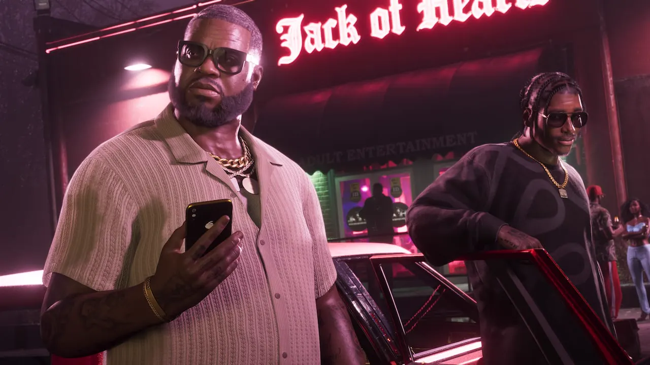 Boobie y Dre'Quan salen de un coche. Boobie sostiene su teléfono mientras Dre'Quan se apoya en la puerta abierta del coche.
