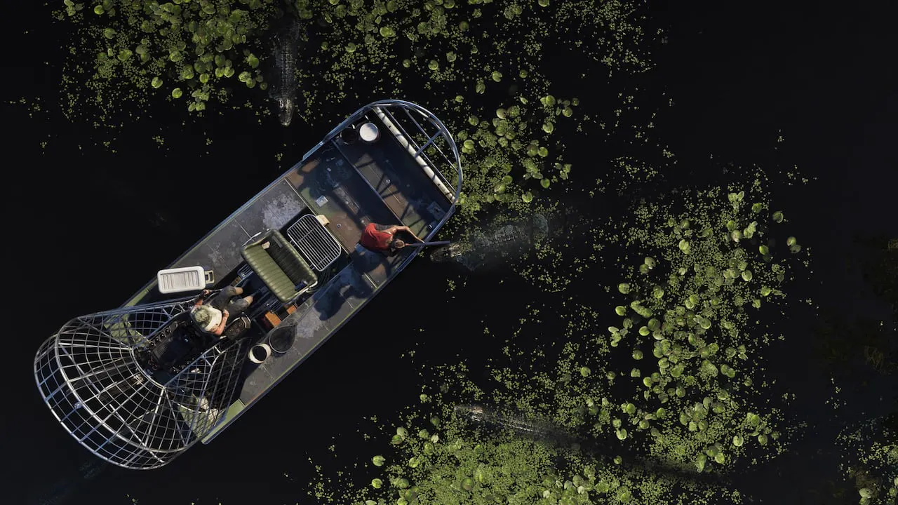 Vista cenital de dos personas en un hidrodeslizador rodeadas de caimanes en Grassrivers. Una de ellas apunta con un arma al caimán más cercano a ella.